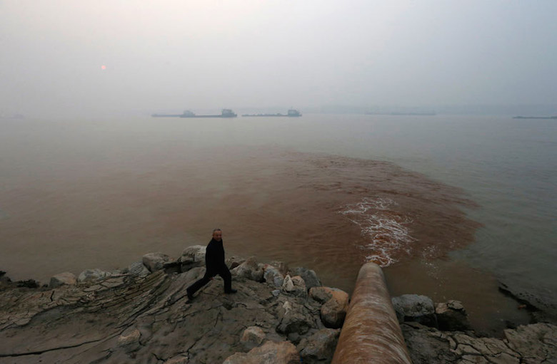 A man walks by a pipe discharging waste water into the Yangtze River, China