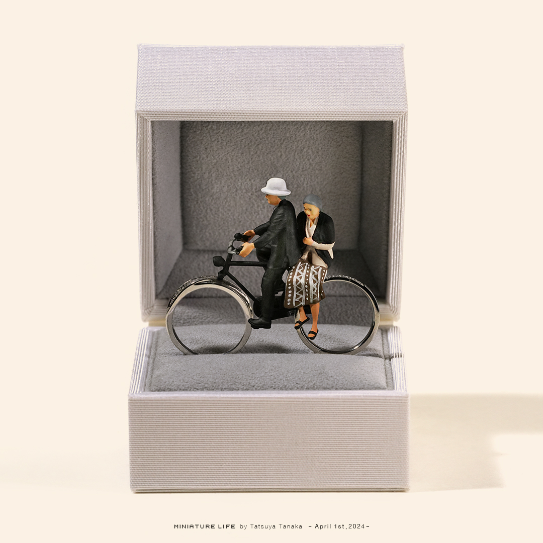 Miniature couple riding a bicycle displayed inside an open jewelry ring box