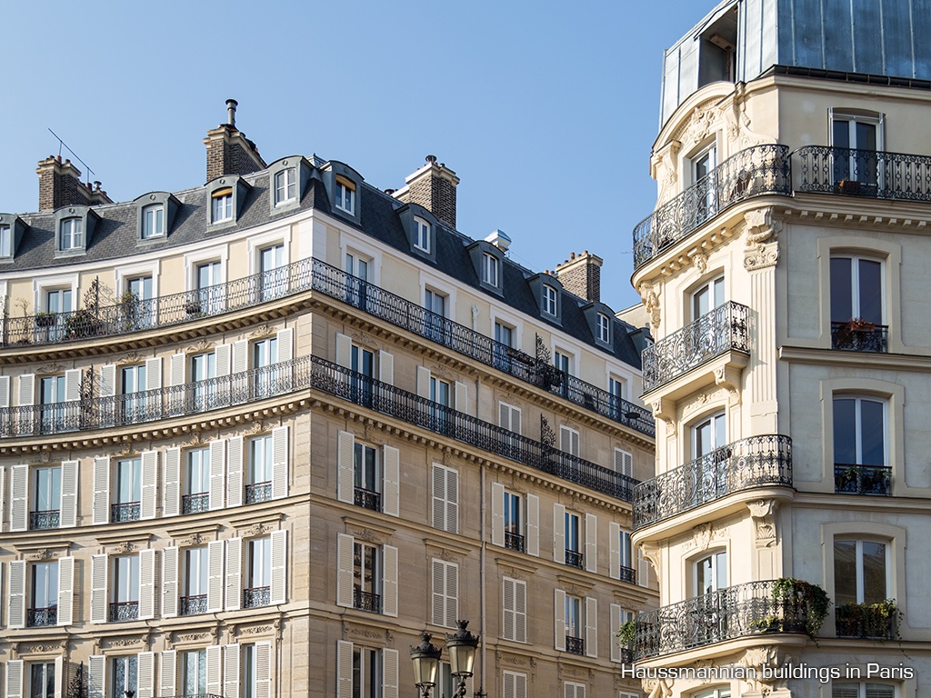 Haussmannian apartment buildings in Paris with uniform cream stone facades, mansard roofs and iron balconies