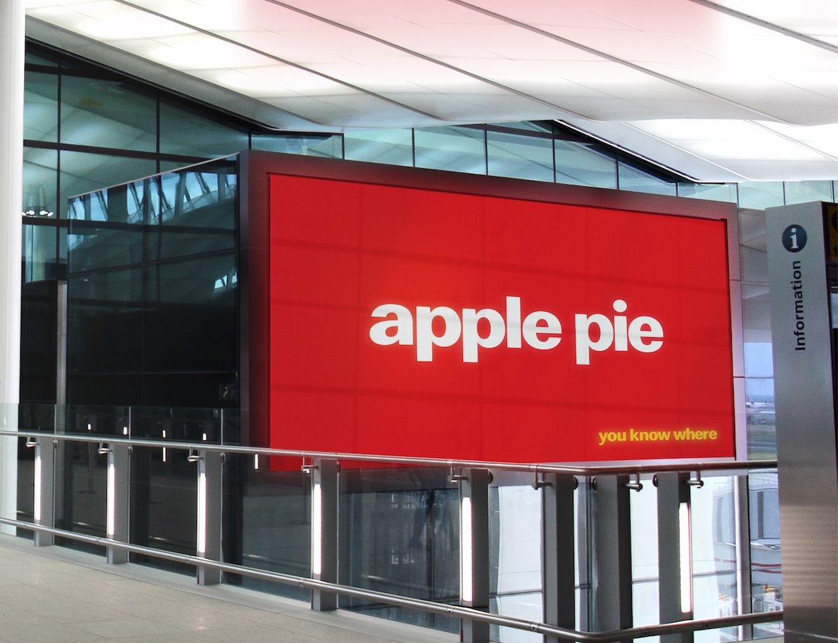 Large red airport billboard reading “apple pie” with “you know where” in yellow, part of a logo-free McDonald’s campaign.