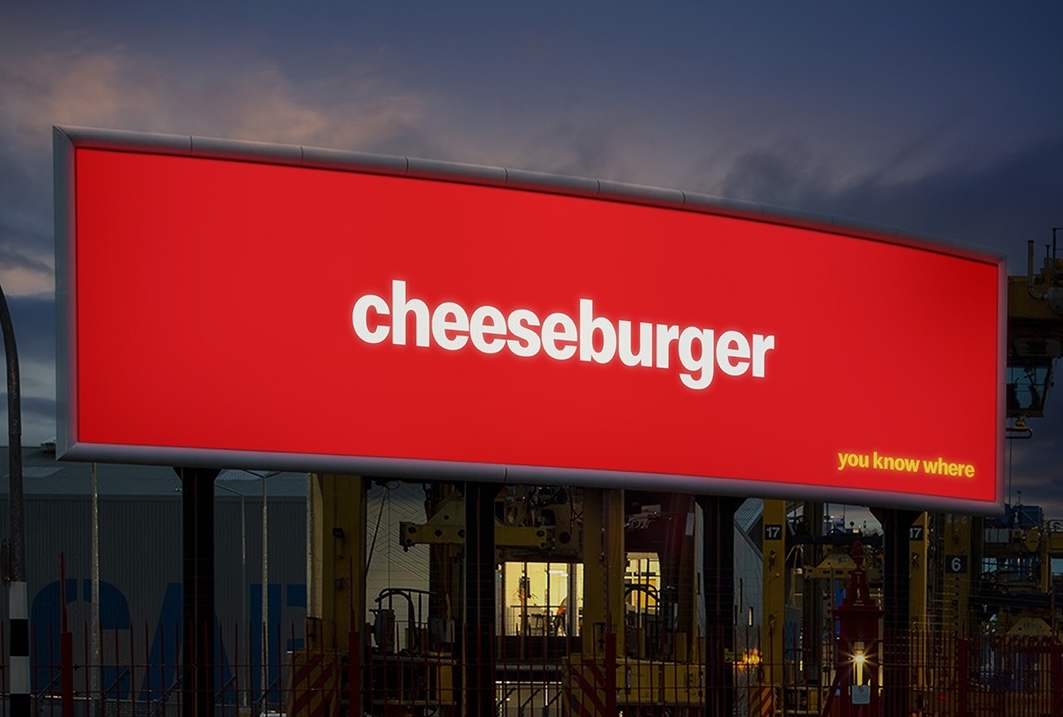 Red billboard showing the word “cheeseburger” with the line “you know where” in yellow, part of a McDonald’s logo-free outdoor ad campaign.