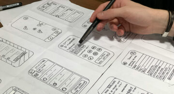 Person reviewing mobile app wireframes with a pen, focused on payment interface design.