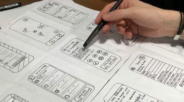 Person reviewing mobile app wireframes with a pen, focused on payment interface design.