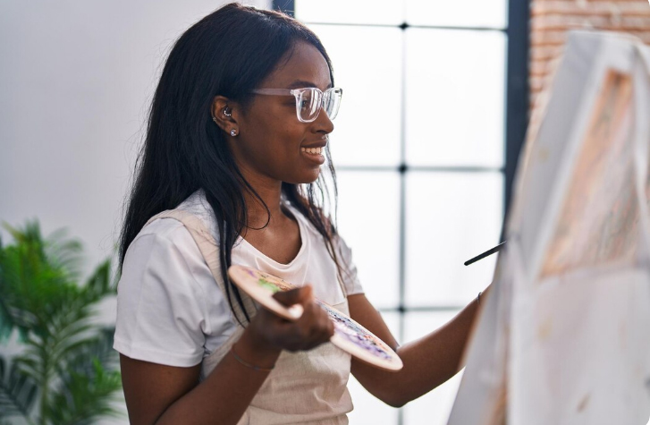 Woman smiling and painting on a canvas using a custom paint-by-numbers kit.