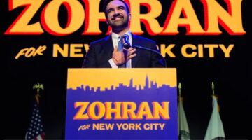 Zohran Mamdani speaking at his campaign event, with bold blue and yellow branding and “Zohran for New York City” typography in the background.