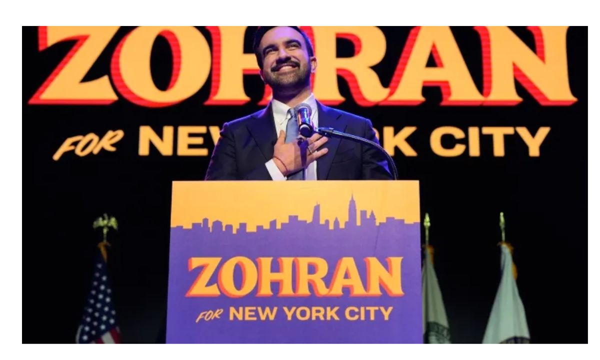 Zohran Mamdani speaking at his campaign event, featuring bold blue and yellow “Zohran for New York City” branding.
