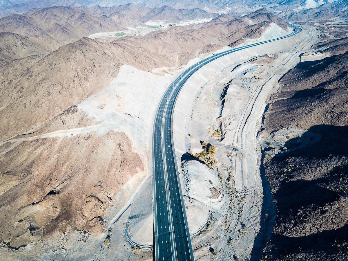 Aerial view of a modern Abu Dhabi highway curving through rocky desert mountains.