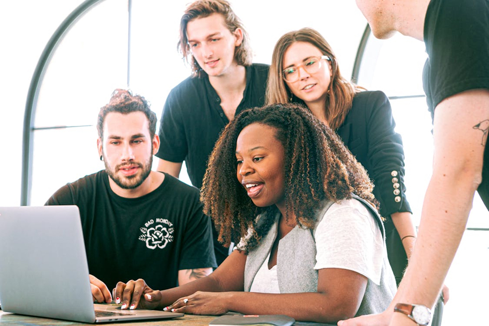 A diverse team collaborating around a laptop during a work meeting.