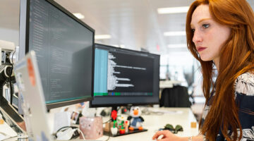 Designer working on a website with code and system structure visible on dual monitors