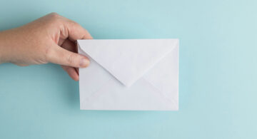Hand holding a white envelope against a blue background symbolizing email communication