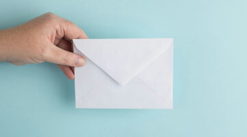 Hand holding a white envelope against a blue background symbolizing email communication