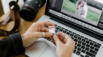 Person holding SD and microSD cards in front of laptop for photo recovery