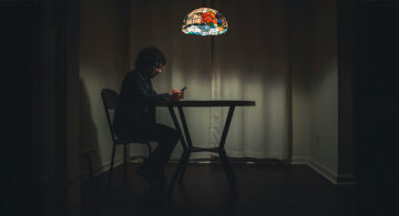 Why Does The Internet Feel Smaller Than It Did A Decade Ago? Man sitting alone in a dark room looking at his phone under a lamp