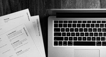 Resume documents and laptop on a wooden desk in black and white