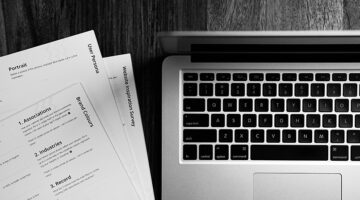 Resume documents and laptop on a wooden desk in black and white